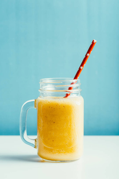 smakelijke mango smoothie in een glazen pot op een blauwe achtergrond - Foto, afbeelding