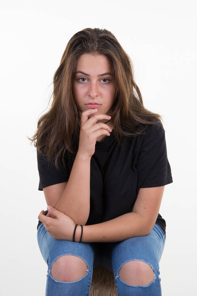 Портрет сердитої дівчини-підлітка, що сидить з руками схрещеною рукою на підборідді на білому тлі
 - Фото, зображення