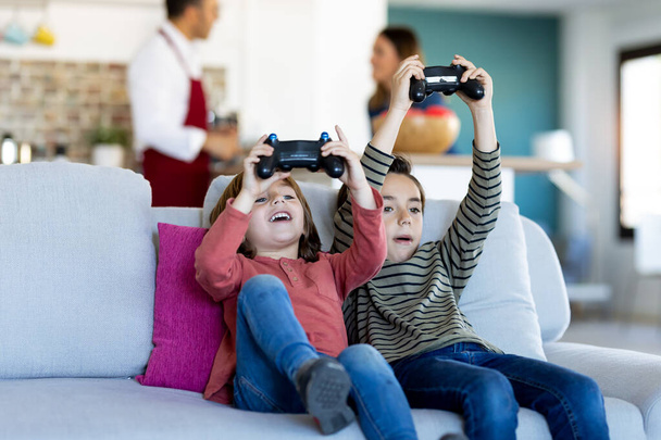Girato di due simpatici fratelli che giocano ai videogiochi seduti sul divano di casa
. - Foto, immagini