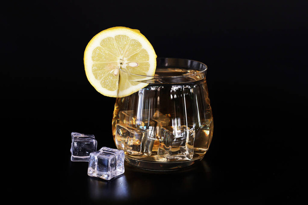 прозрачное стекло с лимонным чаем, льдом и ломтиком лимона на черном фоне
 - Фото, изображение
