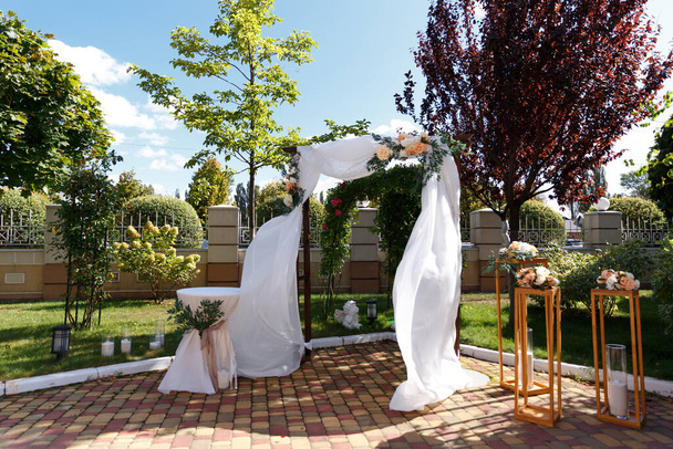 Holzhochzeitsbogen dekoriert mit weißem Tuch und Blumen mit viel Grün steht im Zentrum der Trauung. - Foto, Bild