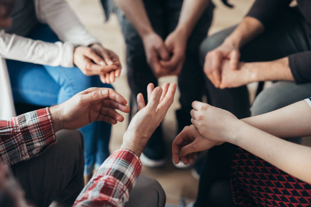 Close-up of hands of people sitting in a circle during a therapy group meeting - 写真・画像
