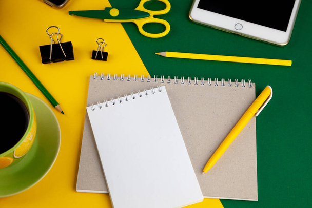 Stationery on the table top view. Yellow and green bright background. Notepad for notes with place for text. Work at home. A cup of coffee. Layout with scissors, pen, notebook. Study and workflow. - Zdjęcie, obraz