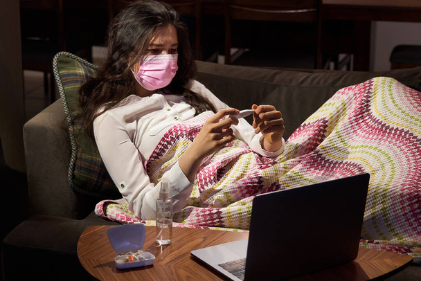 young woman holding thermometer on sofa got fever, caught, sick girl having influenza symptoms, flu or virus concept - Photo, Image
