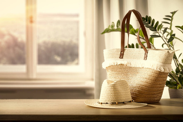 Window with sunlight and summer bag with hat. on the table. - Фото, изображение