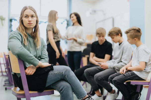 Pretty thoughtful teenage girl sits on the side of a group during extracurricular activities at school - Photo, Image
