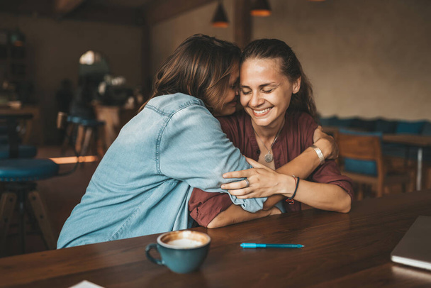 Happy young woman hugging her best friend, sitting in a cafe, having pleasant talk. - Fotoğraf, Görsel