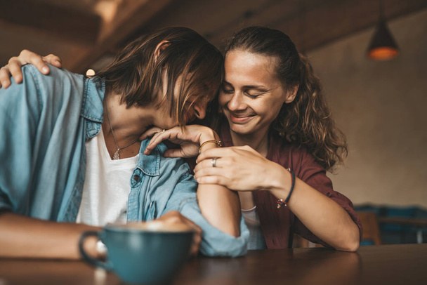 Happy young woman hugging her best friend, sitting in a cafe, having pleasant talk. - Фото, зображення