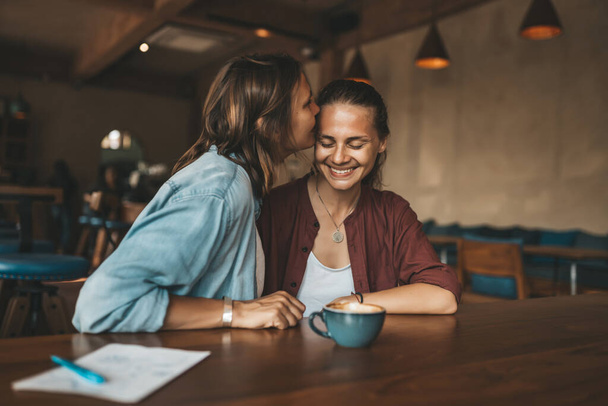 Happy young woman kissing her girlfriend, sitting in a cafe. Happy lesbian couple in love. - Foto, immagini