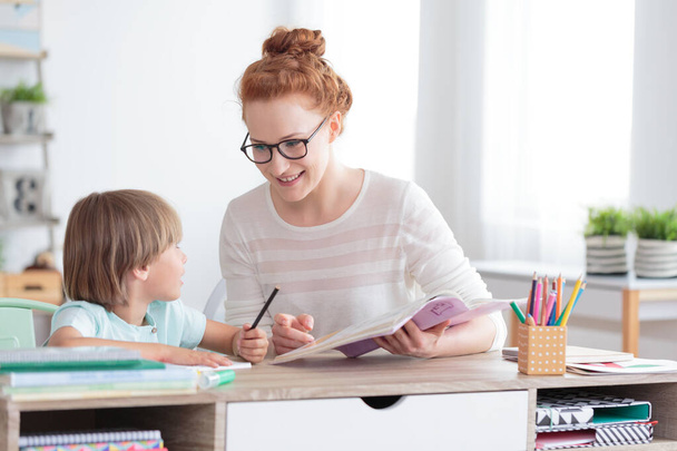 Happy mother and smiling son doing homework at desk - Фото, изображение