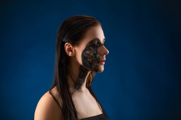 Porträt einer jungen sinnlichen brünetten Frau mit schwarzem Rabenvogel Körperkunst im Gesicht. - Foto, Bild