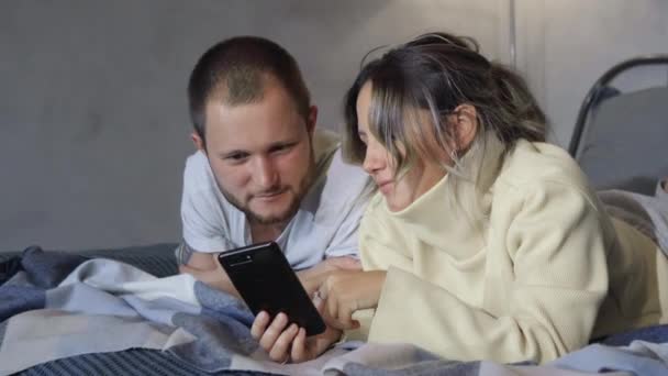 Ehepaar liegt mit Smartphone im Bett Ehepaare, die auf dem Bett liegen und auf Smartphones gucken. Kommunikation in sozialen Netzwerken. Mann und Frau liegen zu Hause im Bett - Filmmaterial, Video