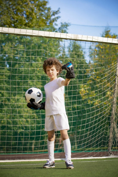 Children are a soccer champion. Boy goalkeeper in football sportswear with a formidable view of the stadium with the ball. Athletic and athletic anger concept. - Φωτογραφία, εικόνα