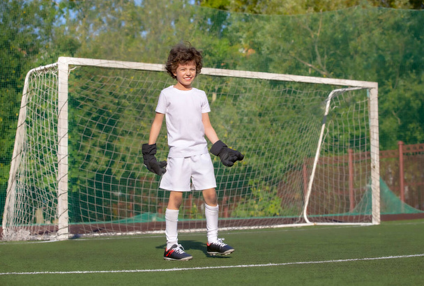 Summer soccer tournament for young kids. football club. emotions and joy of the game. Young goalie. Kids - soccer champion. Boy goalkeeper in football sportswear on stadium with ball. Sport concept. - 写真・画像