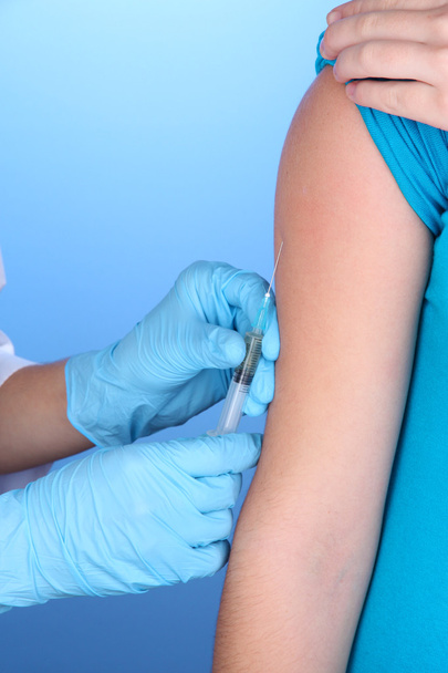 doctor holding syringe with vaccine into patient's shoulder on blue background - Fotoğraf, Görsel