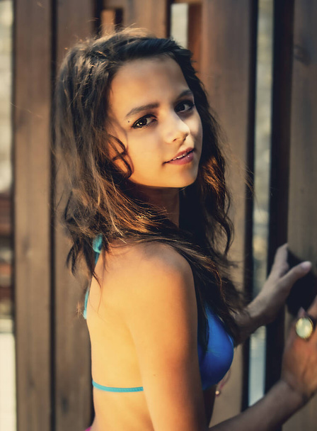 Portrait of a beautiful young girl in blue swimsuit leaned against a wooden fence. - Foto, Bild