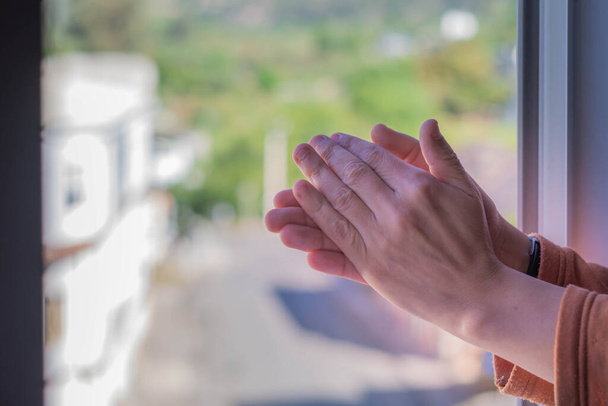 Foto das mãos de uma mulher batendo palmas de sua janela para apoiar aqueles que lutam contra o coronavírus
 - Foto, Imagem