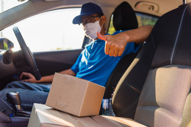 Asian Young delivery man courier online with boxes with uniform sitting in driving car he protective face mask, service customer on front house under curfew quarantine pandemic coronavirus COVID-19 - Fotoğraf, Görsel