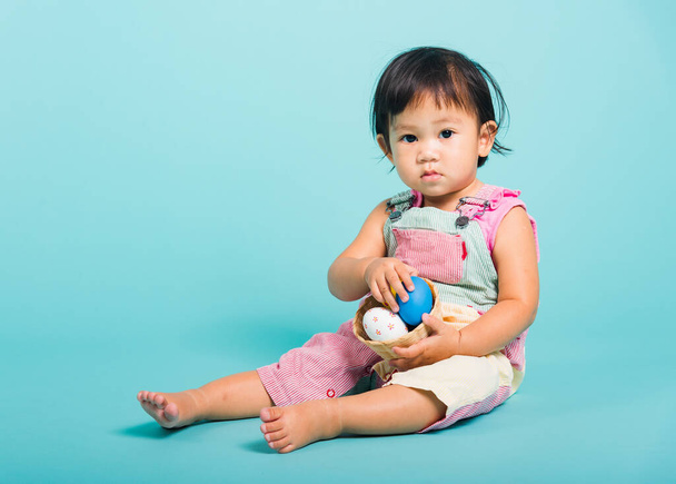 Asian Cute little baby girl beautiful holding Easter egg in basket, studio shot on blue background with copy space, Easter day concept - Foto, imagen