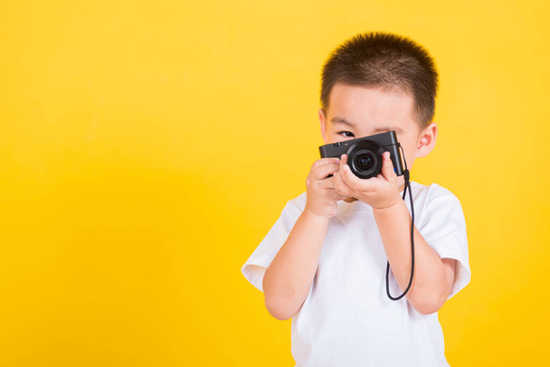 Asian Thai happy portrait cute little cheerful child boy hold photo camera compact doing taking the picture, studio shot isolated on yellow background with copy space - Foto, afbeelding