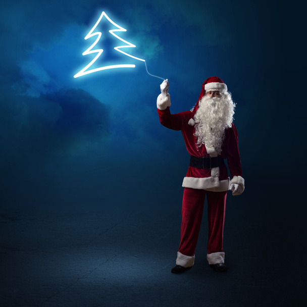 Санта-Клаус держит сияющую елку
 - Фото, изображение