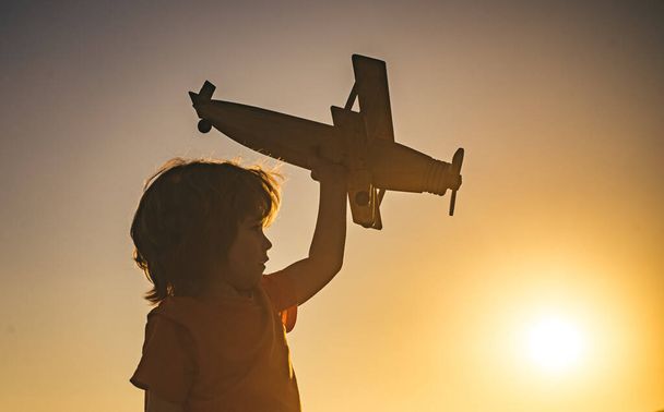 Dreaming boy with wooden plane. Kid boy playing with toy airplane at sunset. Child dreams of traveling and playing with an airplane, pilot aviator in outdoor in the summer. - Photo, Image