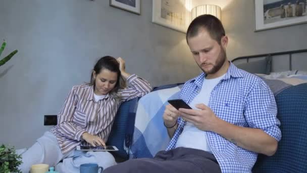 Happy young family couple holding phone looking at screen taking sit on floor in modern room apartment, man and woman at home - Filmagem, Vídeo