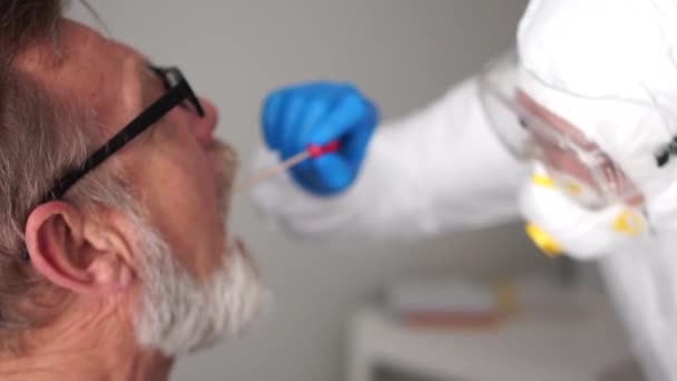 Close up portrait of a doctor in a protective suit takes a swab from the throat of an elderly senior man pensioner. Non-invasive diagnostic method by PCR reaction - 映像、動画