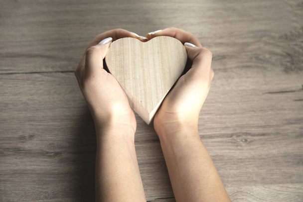 main de femme tenant coeur en bois sur la table
 - Photo, image
