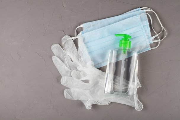 Концепция коронавируса, одноразовые перчатки, медицинские маски и антисептики лежат на сером фоне
 - Фото, изображение