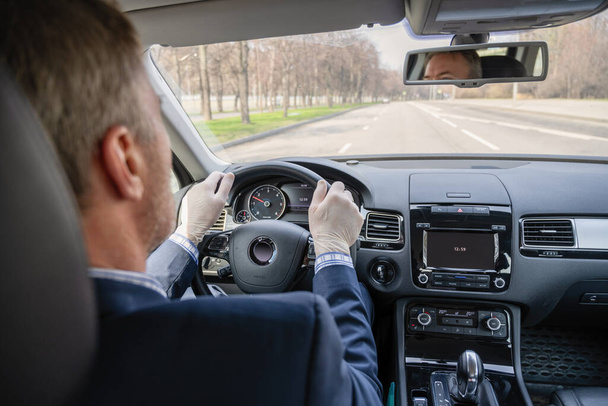 Middle age businessman in a blue suit and rubber gloves for protect himself from bacteria and virus driving a car. Coronavirus. Pandemic. - Foto, Bild