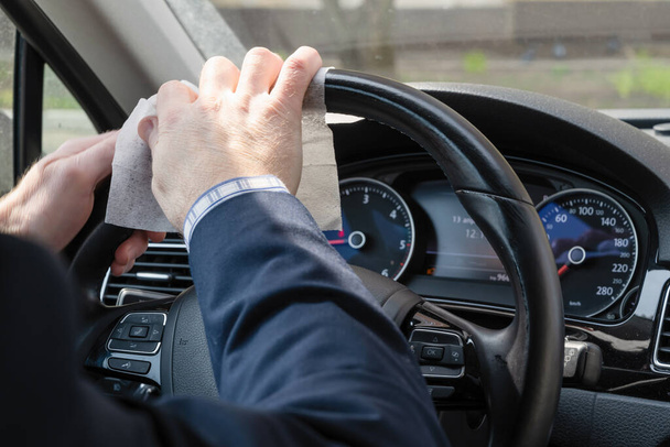 Middle age businessman in a blue suit cleaning steering wheel of a car using antivirus antibacterial wet wipe (napkin) for protect himself from bacteria and virus - Photo, image