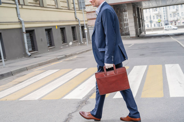 Allein der grauhaarige Geschäftsmann mittleren Alters im blauen Anzug mit Aktentasche lacht beim Telefonieren auf dem Fußgängerüberweg in der Stadtstraße. - Foto, Bild