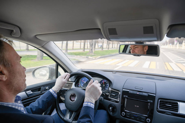Middle age businessman in a blue suit and rubber gloves for protect himself from bacteria and virus driving a car. Coronavirus. Pandemic. - Foto, imagen