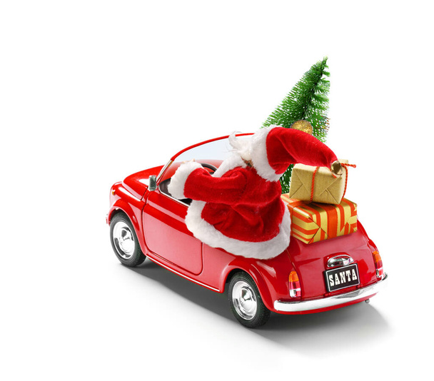 Санта-Клаус за рулем красной машины с подарочными коробками и елкой изолированы на белом, вид снаружи
 - Фото, изображение