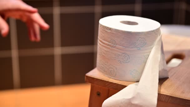 Close-up beeld van de toiletrol. De rechterhand van een blanke man probeert de rol papier te grijpen, hij kan er niet bij en hij wanhoopt door zijn vuist te maken. - Video