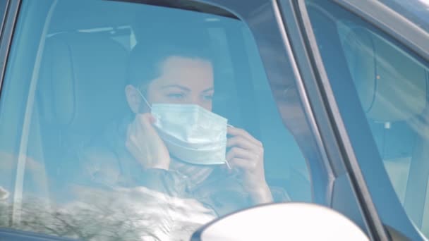 Vrouw in de auto zet gezichtsbescherming masker en het openen van autoraam. Coronavirus - Video