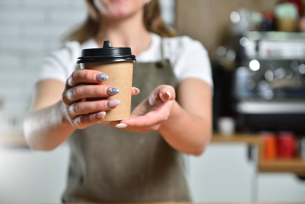 Young girl bartender barista holds out his hand with a paper cup of takeaway coffee. - Fotoğraf, Görsel