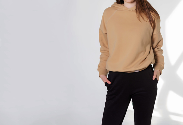 Young girl wearing blank sweatshirt and and sport pants. Gray wall background shadow light from the window with copy space for your text message or promotional content - Foto, Imagem