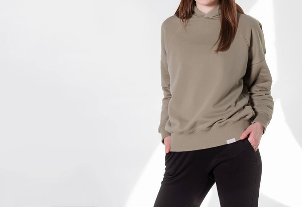 Young girl wearing blank sweatshirt and and sport pants. Gray wall background shadow light from the window with copy space for your text message or promotional content - Zdjęcie, obraz