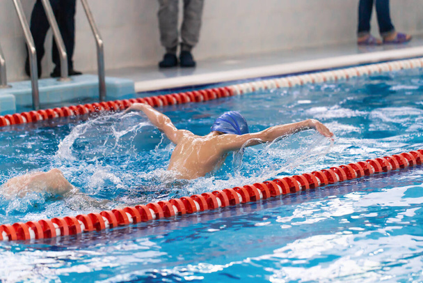 Úszómedence sportoló edzés beltéri szakmai verseny. Tini úszó, aki pillangóúszást végez a beltéri úszóversenyen. - Fotó, kép