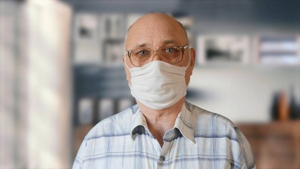 Пожилой человек в домашней защитной маске ручной работы в помещении
 - Фото, изображение