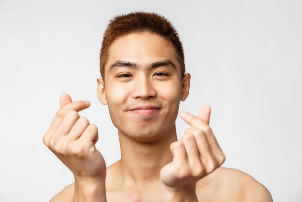 Beauty, skincare and men health concept. Close-up portrait of happy handsome asian naked man, showing korean love signs and smiling, express sympathy or like, white background - Fotografie, Obrázek