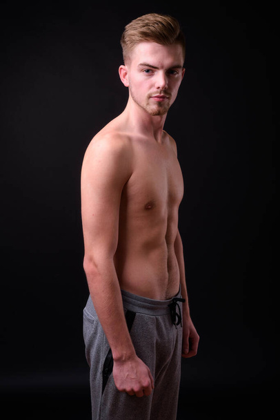 Studio shot of young handsome man shirtless against black background - Photo, image