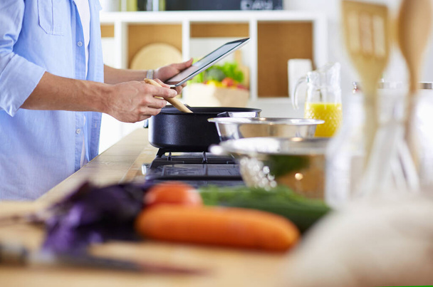 Homme suivant la recette sur tablette numérique et la cuisine savoureuse et saine dans la cuisine à la maison - Photo, image