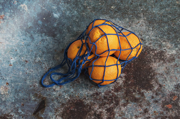 Oranges in an eco-netted blue bag on a dark background. Environmental care, waste recycling - Foto, afbeelding