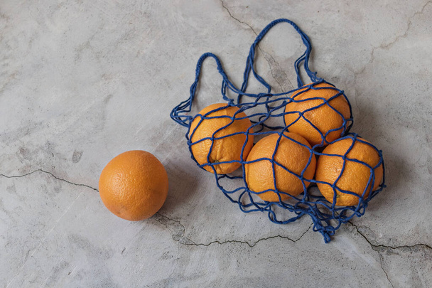 Pomarańcze w ekologicznej niebieskiej torbie na szarym tle. Ochrona środowiska, recykling odpadów - Zdjęcie, obraz
