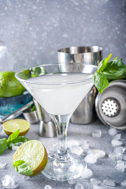 Bazylia wódka gilet martini koktajl. Mocny napój alkoholowy ze świeżą bazylią, limonką i wódką w klasycznym kieliszku martini, miejsce na kopię w tle z szarego kamienia - Zdjęcie, obraz