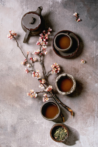 Tea drinking wabi sabi japanese style dark clay cups and teapot with blooming cherry branches. Grey texture concrete background. Flat lay, space - Fotó, kép
