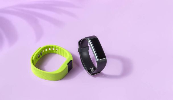Activiteit slimme trackers op lichtroze achtergrond. Zwart en groen fitness horloge, sport armbanden - Foto, afbeelding